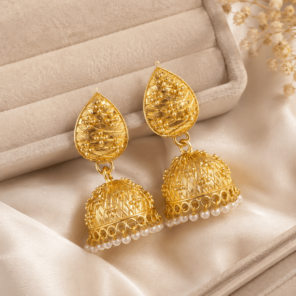 Gold-tone teardrop jhumka earrings with pearl bead dangle fringe, lying on fabric