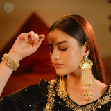 Woman wearing gold jewelry including earrings and a bracelet against a warm-toned background.