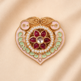 An ornate heart-shaped brooch featuring gold-plated metalwork, pink enamel, light green enamel, white faux pearls, and a central cluster of red gemstones, displayed on a soft beige satin background.
