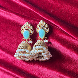 Ornate gold earrings with turquoise stones and pearl-like beads on a red velvet background