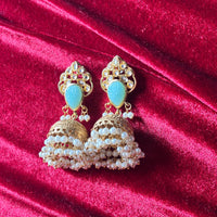 Ornate gold earrings with turquoise stones and pearl-like beads on a red velvet background