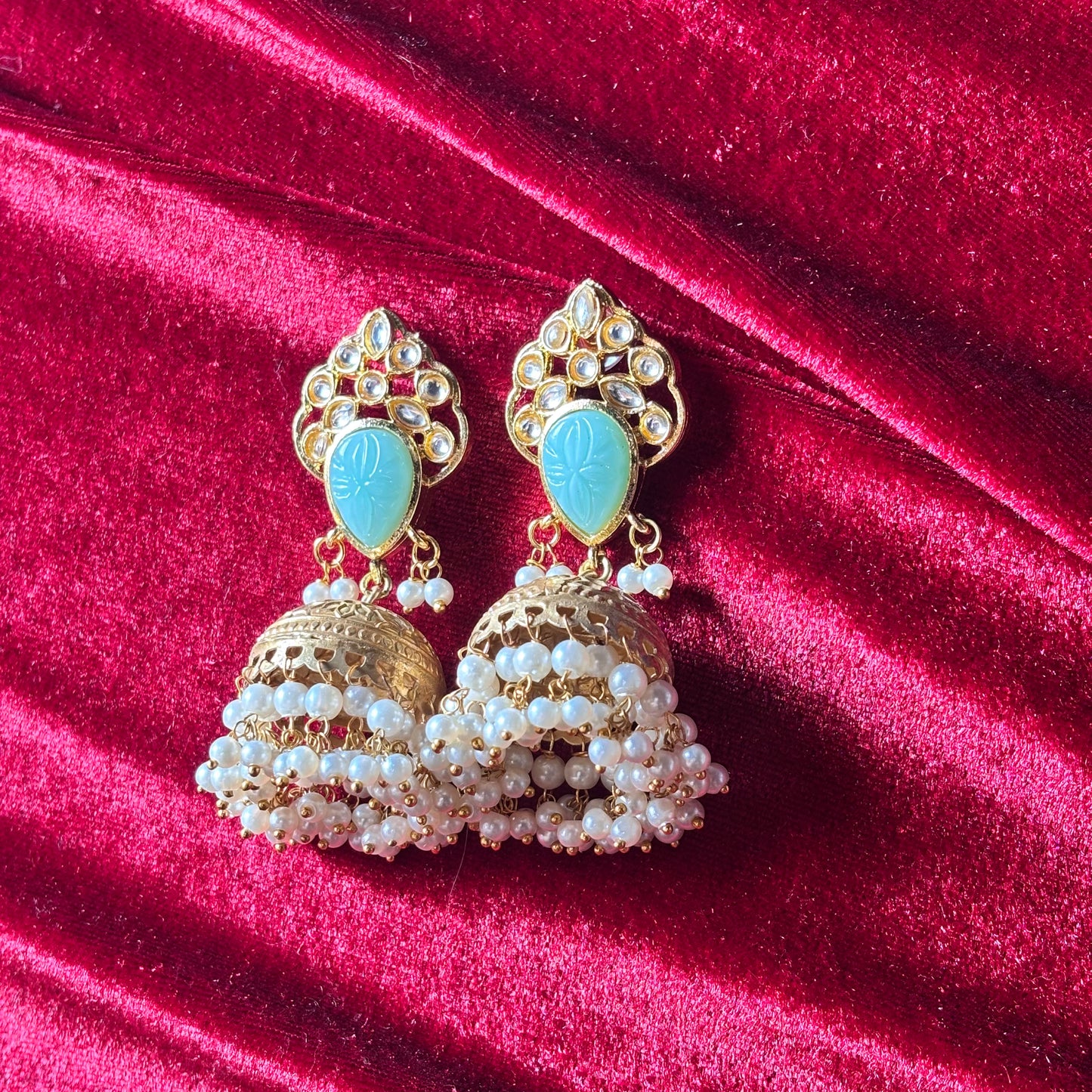 Ornate gold earrings with turquoise stones and pearl-like beads on a red velvet background