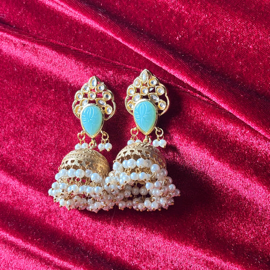Ornate gold earrings with turquoise stones and pearl-like beads on a red velvet background