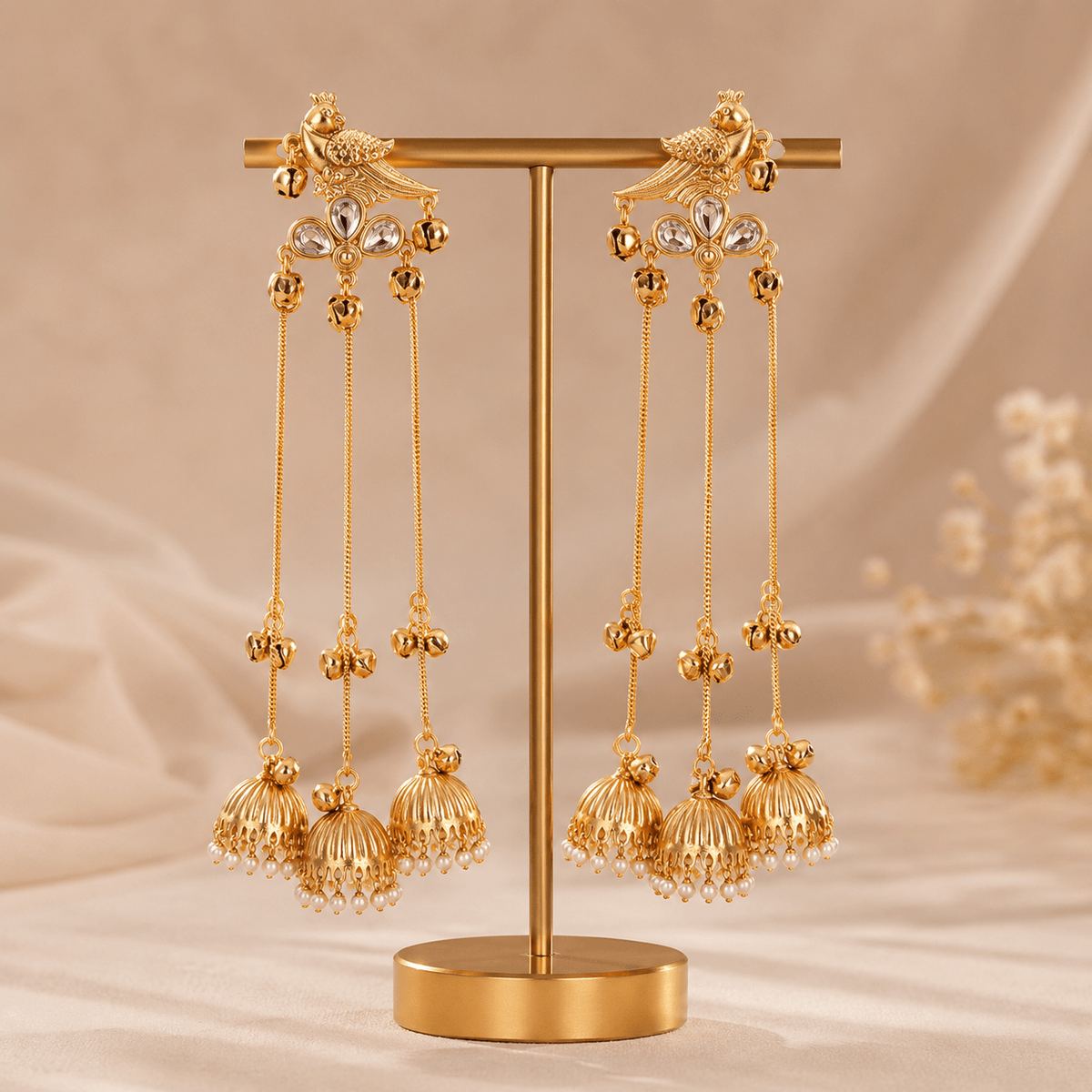 Gold-tone bird motif jhumka drop earrings on display stand, long chain tassels