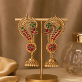 Gold-tone peacock jhumka earrings on display stand, green and magenta enamel, pearl drops.