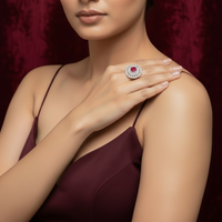 Close-up of a hand wearing a ring with a red gemstone and diamond accents, set against a red velvet background.
